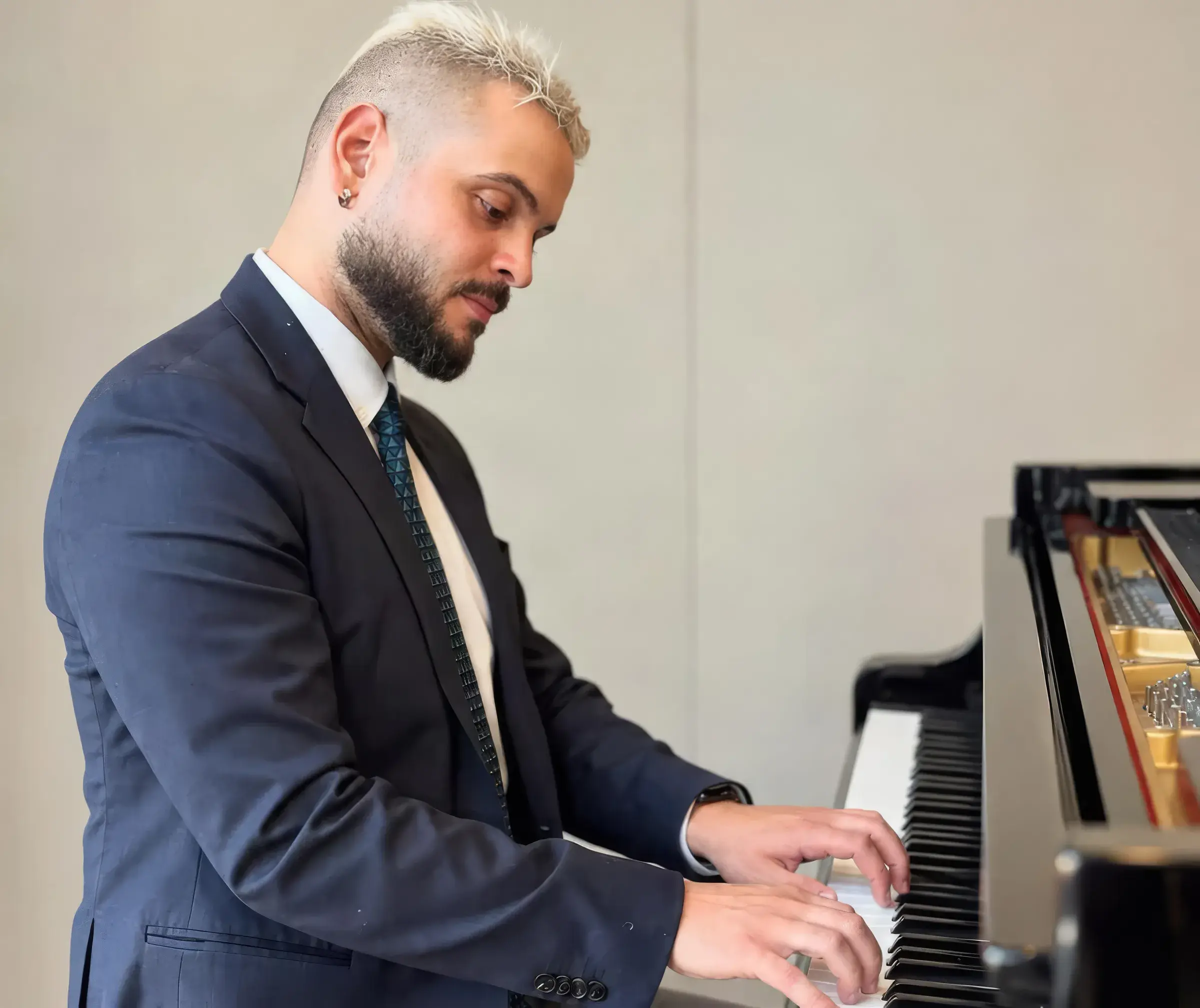 A pianist at a grand piano, hands on the keys, in a jacket and tie