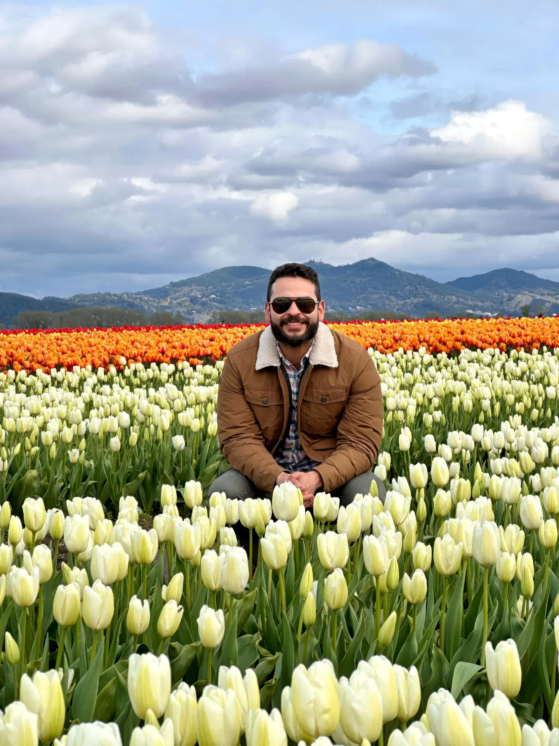 Johnson Gouvêa sitting among rows of white and orange tulips, with forested mountains behind