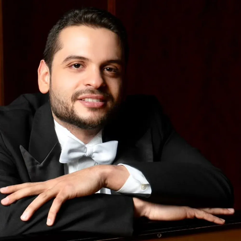 Portrait of Johnson Gouvêa in white tie, leaning on a grand piano