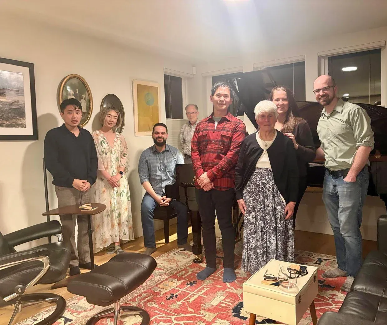 Adult students and guests gathered around a grand piano in a living room after a studio recital