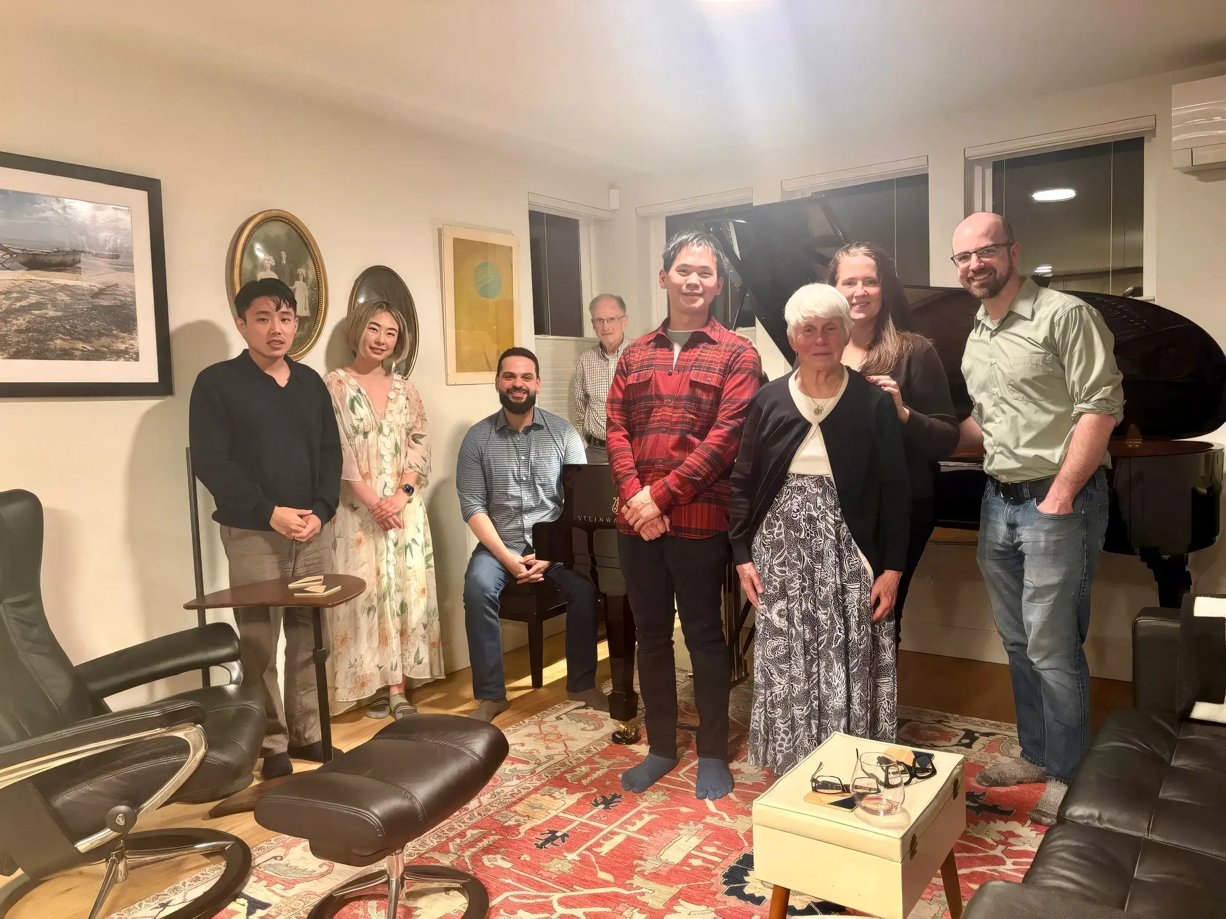 Adult students and guests gathered around a grand piano in a living room after a studio recital